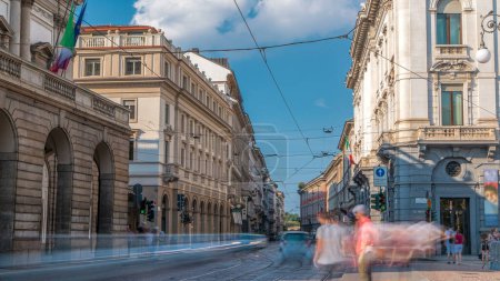 Photo for Traffic on Alessandro Manzoni street near main concert hall of Teatro alla Scala, an opera house timelapse in Milan, Italy. Blue cloudy sky at summer day. Tram tracks - Royalty Free Image