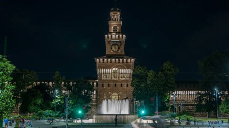 Photo for Main entrance to the Sforza Castle and tower - Castello Sforzesco illuminated at night timelapse, Milan, Italy. Fountain and traffic lights - Royalty Free Image