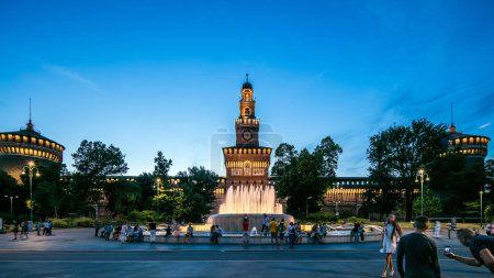 Photo for Main entrance to the Sforza Castle front view and tower - Castello Sforzesco illuminated day to nigh transition timelapse, Milan, Italy. Fountain and people walking around - Royalty Free Image