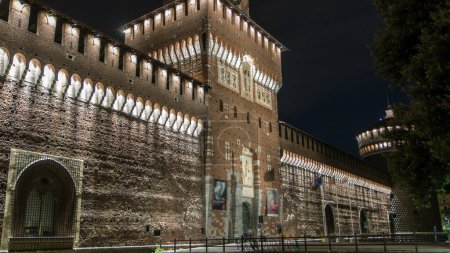 Photo for Main entrance to the Sforza Castle and tower - Castello Sforzesco illuminated at night timelapse, Milan, Italy. Side view - Royalty Free Image