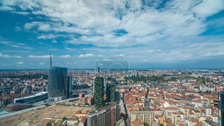 Téléchargez les photos : Milan vue panoramique aérienne des tours et gratte-ciel modernes et de la gare de Garibaldi dans le quartier des affaires timelapse fiew de toit. Maisons avec des toits rouges. Ciel bleu nuageux le jour d'été - en image libre de droit