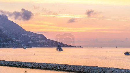 Sea and landscape timelapse from Beaulieu sur mer during sunrise, France. Boats and yachts on foreground. Reflections on water and colorful sky