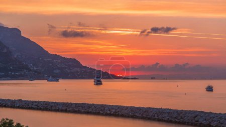 Sunrise view of sea and landscape timelapse from Beaulieu sur mer, France. Boats and yachts on foreground. Sun raised behind clouds. Reflections on water.