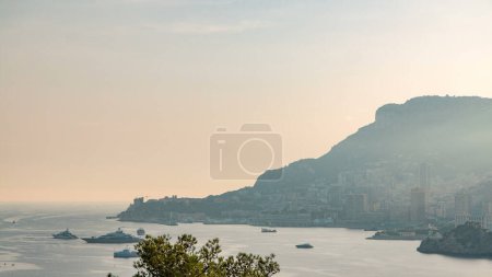 Téléchargez les photos : Timelapse paysage urbain de Monte Carlo, Monaco pendant le coucher du soleil d'été. Rayons de soleil couchant avec brume du soir. Yachts sur le port. Vue aérienne du Cap Martin - en image libre de droit
