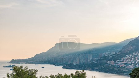 Panoramic cityscape timelapse of Monte Carlo, Monaco during summer sunset. Rays of setting sun with evening mist. Yachts on harbor. Top view from Cap Martin