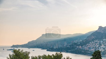 Téléchargez les photos : Paysage urbain panorama intemporel de Monte Carlo, Monaco pendant le coucher du soleil d'été. Rayons de soleil couchant avec brume nocturne. Yachts dans le port. Vue de dessus depuis Cap Martin - en image libre de droit