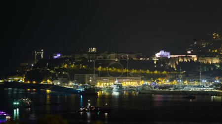 Foto de Paisaje urbano de Monte Carlo en horario nocturno, Mónaco. Niebla nocturna e iluminación nocturna de edificios con Palacio Principesco. Yates en el puerto. Vista superior desde Cap Martin - Imagen libre de derechos