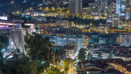 Téléchargez les photos : Panorama de Monte Carlo près du château la nuit depuis la plate-forme d'observation dans le village de Monaco près de Port Hercule. Toits de maisons et de bâtiments avec éclairage et collines sur fond aérien - en image libre de droit