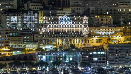 Monte Carlo with hotels timelapse at night from the observation deck in the village of Monaco with Port Hercules. Buildings with illumination and yachts in harbor aerial top view. Traffic on the road