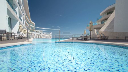 Téléchargez les photos : Hôtel petite piscine avec des reflets ensoleillés et timelapse de l'eau bleue, vue sur la plage de Sesimbra, Portugal - en image libre de droit
