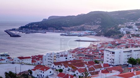 Crepúsculo después de la puesta de sol en Sesimbra, Portugal timelapse de día a noche transición cuando las luces se encienden panorama. Muelle en una playa
