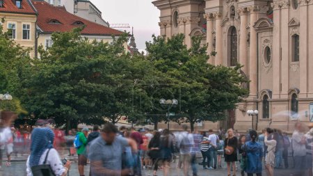 Téléchargez les photos : L'église Saint-Nicolas derrière les arbres timelapse à Prague, République tchèque. Personnes marchant sur la Place de la Vieille Ville - en image libre de droit