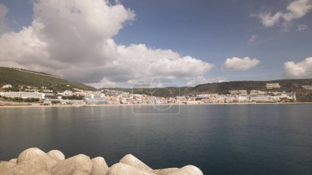 Foto de Panorama que muestra la vista de la ciudad de Sesimbra y Port timelapse, Portugal. Paisaje del horizonte con barcos, casas y playa desde el faro en un muelle. Resort en el distrito de Setubal. Hermosas nubes - Imagen libre de derechos