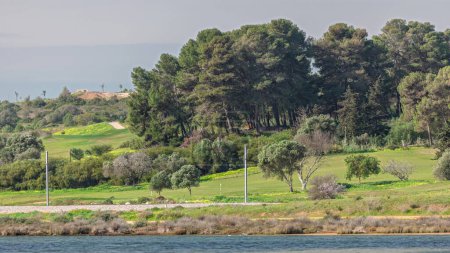 Téléchargez les photos : Terrains de golf modernes pour les touristes avec des étangs clairs et des palmiers pour la détente et le golf timelapse. Lagos, Portugal, Algarve. Journée ensoleillée avec des joueurs de golf sur des chariots. Vue rapprochée de l'océan - en image libre de droit