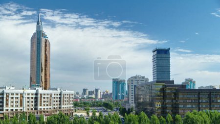 New business district aerial timelapse with traffic on road from mosque roof in the capital of Kazakhstan in Astana. Green trees in park. Nur-Sultan city skyline panorama