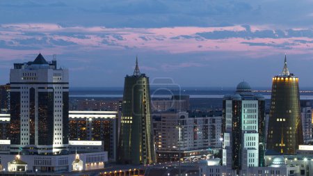 Foto de Vista nocturna elevada sobre el centro de la ciudad y el distrito central de negocios con torres amarillas Timelapse transición día a noche cuando la iluminación se enciende, ciudad de Nur-Sultan, Kazajstán, Asia Central - Imagen libre de derechos