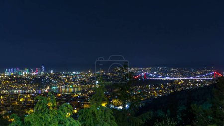 Illuminated Fatih Sultan Mehmet Bridge overview, connects Asia and Europe night timelapse from top of Camlica hill. Istanbul, Turkey. City skyline with skyscrapers on background
