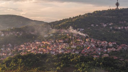 Photo for City panorama with houses, tv tower and mountains from Old Jewish cemetery timelapse in Sarajevo. Skyline with smoke at evening before sunset. Bosnia and Herzegovina - Royalty Free Image