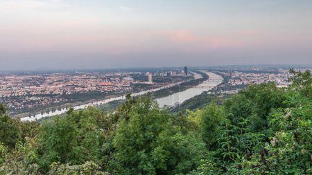 Panoramic skyline of Vienna from Danube Viewpoint Leopoldsberg aerial day to night transition timelapse. Bridges over the river, skyscrapers and historic buildings at evening after sunset