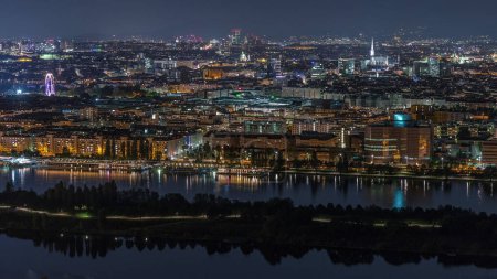 Aerial panoramic view over Vienna city with skyscrapers, historic buildings and a riverside promenade night timelapse in Austria. Illuminated skyline from Danube Tower viewpoint