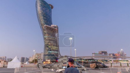 Photo for Abu Dhabi, UAE - Feb 25, 2023: National Exhibition Centre (ADNEC) where IDEX Military Exibition was held day to night transition timelapse, UAE. Outside view with modern skyscraper behind helicopters - Royalty Free Image