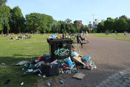 Photo for Rubbish next to rubbish bin in park with recreationists on lawn - Royalty Free Image