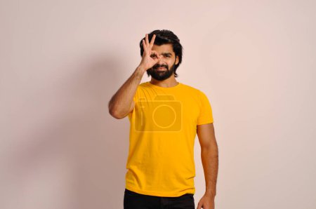 Foto de Joven hermoso hombre asiático vistiendo camiseta amarilla y haciendo buen gesto con la mano sonriendo, los ojos mirando a través de los dedos con la cara feliz. - Imagen libre de derechos