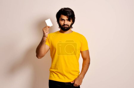 Téléchargez les photos : Jeune homme tenant une carte de crédit, fronçant les sourcils en raison de problèmes. Regard en colère - en image libre de droit