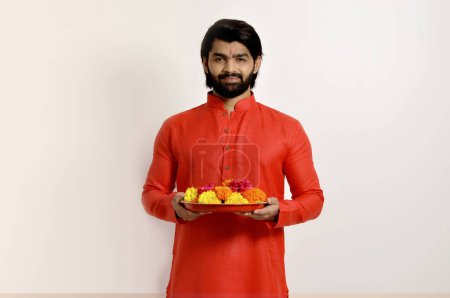 Photo for Young Indian handsome man wearing kurta, side view, holding Flowers thali - Royalty Free Image