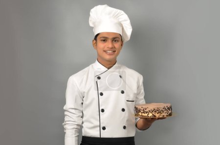 Téléchargez les photos : Portrait d'un heureux chef masculin vêtu d'une assiette de tenue uniforme avec gâteau au chocolat avec pose de magicien - en image libre de droit