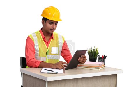 Téléchargez les photos : Architecte indien portant un casque et une veste de sécurité travaillant avec une tablette au bureau. - en image libre de droit