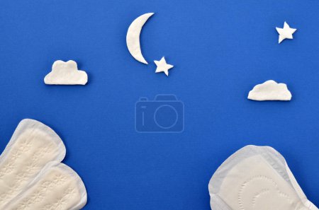 Téléchargez les photos : Women's pads on a blue background and clouds and the moon from cotton wool - en image libre de droit