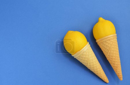 Téléchargez les photos : Concept alimentaire, citrons jaunes dans un cône de gaufre sur fond bleu, espace de copie - en image libre de droit