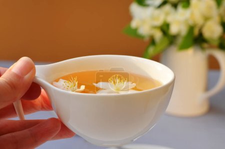 cup with herbal tea and flowers in hand close-up