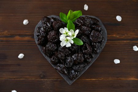 prunes on a heart-shaped board and flower petals flat lay