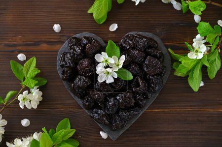 heart-shaped prunes and blossoming plum branches on a wooden background