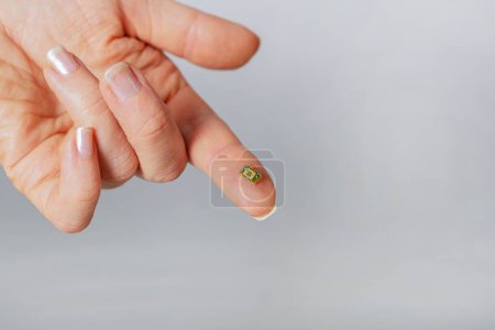 Foto de Microchip pequeño en el dedo de una persona. Conespirología. Control de Población. Poder sobre la gente. Gestión de personas. Nanotecnología. Tecnologías futuras En microbiología Primer plano, sobre un fondo gris, copia - Imagen libre de derechos