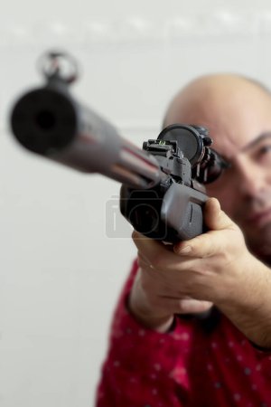 Téléchargez les photos : Vue optique d'une arme traumatique d'un fusil gros plan dans les mains d'un homme visant en arrière-plan hors foyer. - en image libre de droit