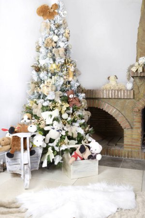 Téléchargez les photos : Fond de Noël, arbre de Noël décoré avec des jouets et des boules de verre près d'une cheminée en pierre avec guirlande d'arbre de Noël décorative et feu de cheminée, tapis molletonné chaud.Décor intérieur de la maison de Noël - en image libre de droit