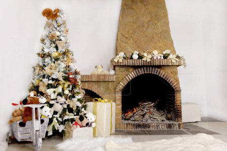Téléchargez les photos : Fond de Noël, arbre de Noël décoré avec des jouets et des boules de verre près d'une cheminée en pierre avec guirlande d'arbre de Noël décorative et feu de cheminée, tapis molletonné chaud.Décor intérieur de la maison de Noël - en image libre de droit