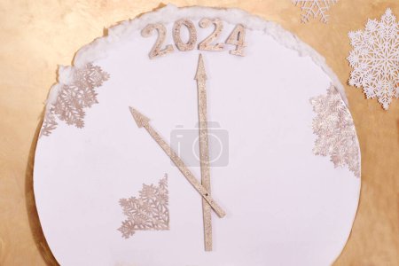 Foto de Reloj decorativo con nieve, copo de nieve, flechas que apuntan a 2024 sobre un fondo en el color del melocotón del año.El concepto del nuevo año, el color de moda del melocotón sombra del año, pantone. - Imagen libre de derechos