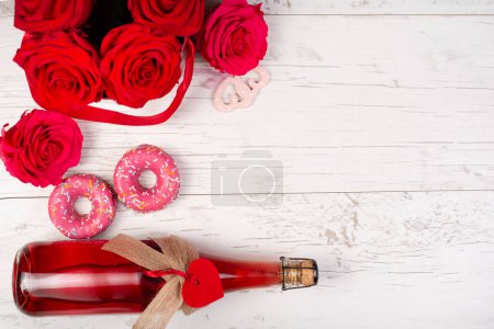 background for Valentine's day with a bottle of champagne, heart, red roses, sweets donuts on a wooden background. Greeting invitation card, mockup