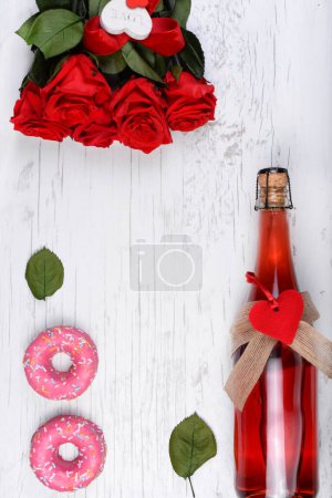 Hintergrund für den Valentinstag mit einer Flasche Champagner, Herz, roten Rosen, süßen Donuts auf einem hölzernen Hintergrund. Grußkarte, Attrappe für Hochzeit, Geburtstag