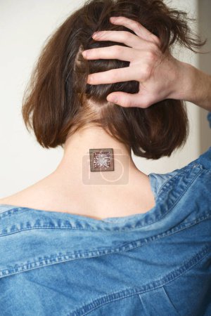 A man shows a microcircuit chip on his neck, holding up his hair. A chipped man. Control, modification of health using nanotechnology. Implanted micro technology. Photo taken with a camera