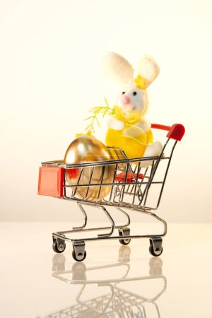 Shopping trolley with a golden egg and a toy hare, Easter bunny. Buying and increasing the price of colored eggs for Easter. Preparation for the holiday.