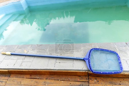 A hand-held cleaner of a large garbage collection net lies on the edge of the pool. Cleaning service. Preparation for summer season