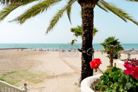 Idyllic view of the Mediterranean beach from an ancient staircase with people relaxing in the distance. Azure sea and coastline with tropical plants, view from a seaside hotel.     CREATED USING A CAMERA NIKON,  WITHOUT the use of AI