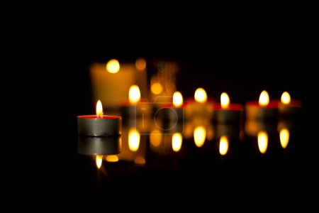 The flickering lights of candles in memory of the deceased In the silence of the darkness of the funeral, reflected on the memorial plaque. Sad mourning background