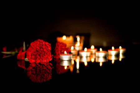 Flores rojas de clavel y muchas velas encendidas en memoria del difunto del funeral. Triste fondo de luto