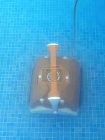 Robot aspirateur à eau nettoie, enlève les débris sur le fond, les murs de la piscine, vue de dessus à travers l'eau translucide. Processus de nettoyage de piscine. Préparation de la saison estivale. Technologies de la maison intelligente